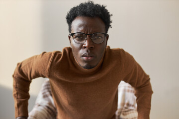 Obraz premium What did you say? Puzzled indignant young African male in glasses frowning eyebrows, having frustrated or displeased facial expression, being suspicious of something. Human attitude and perception