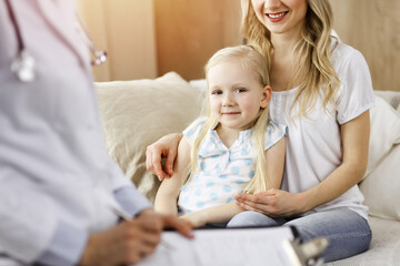 Doctor and patient in sunny room. Pediatrician using clipboard while examining little girl with her mother at home. Medicine concept