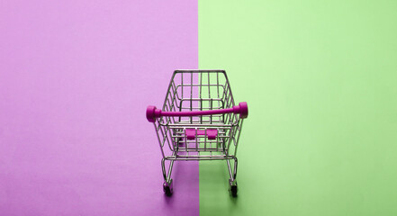 Mini supermarket trolley on a green-pink pastel background. Shopping concept