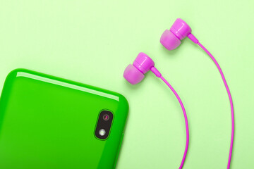 Green Smartphone with vacuum earphones on green background. Top view