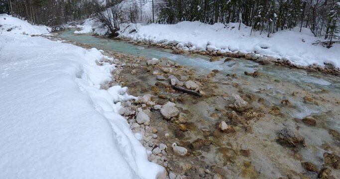 Colorful Sava Dolinka river flowing in Vrata valley, Slovenia. Alpine river flowing downstream in winter season. Snowy landscape. Tilt up, real time, wide angle