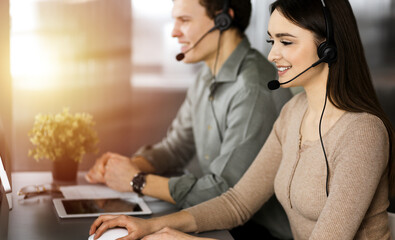 Call center operators at work. Two young people in headsets are talking to the clients, while sitting in sunny office