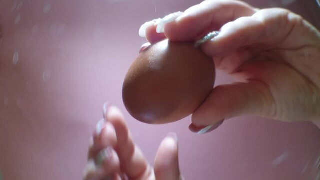 a woman's hand holds an egg and breaks it with a knife, a view of the broken egg from below