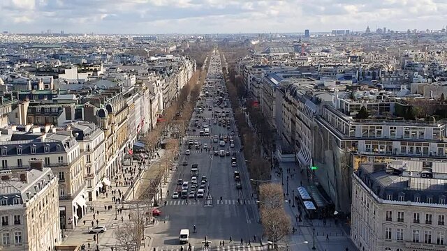 Moving traffic on famous Avenue des Champs-Elysees in Paris, France from above. Parisian skyline with classical French buildings and blue sky. Cars drive on road, people walk. Autumn or winter time