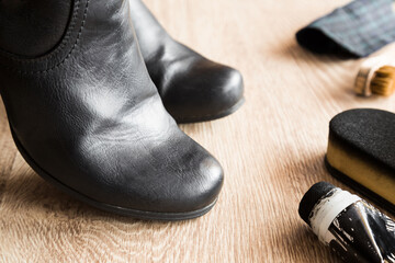Black classic leather boots and cleaning set on wooden floor background. Care about boots beauty and protection from cold and wet. Preparing for autumn and winter season. Closeup.