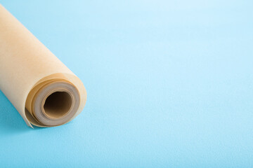 Roll of baking paper on light blue table background. Pastel color. Closeup. Empty place for text.