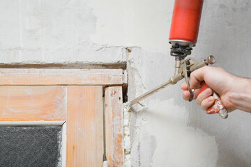 Young adult man hand using spray gun and filling gap with construction foam between old door frame...