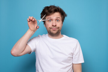 Caucasian shaggy man trying to make a hairstyle by himself with scissors.
