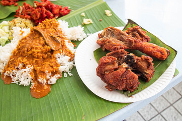 Traditional South Indian Meal Served on Banana Leaf. White rice with curry, chicken fried and fried bitter gourd