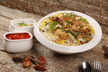 chicken biryani with pickle and yoghurt garnished with spices stone background 