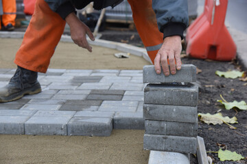 A worker takes concrete paving slabs, lays them on the sand,and builds a parking lot.