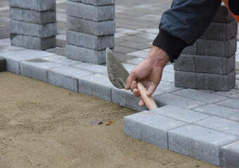 The builder levels the road tiles laid out on the sand.