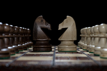 Chess faceoff of both knights horses on top of a chess board in front of a black background...