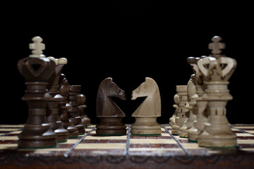 Chess faceoff of both knight horses on top of a chess board in front of a dark background...