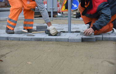 Two workers are laying paving slabs, building a parking lot for cars.