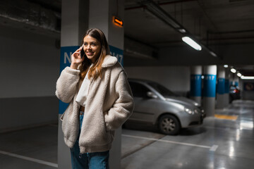 Fototapeta premium Positive fashionable girl in underground parking talking on the phone