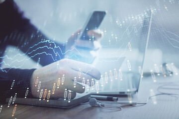 Double exposure of man's hands holding and using a phone and financial graph drawing. Analysis concept.