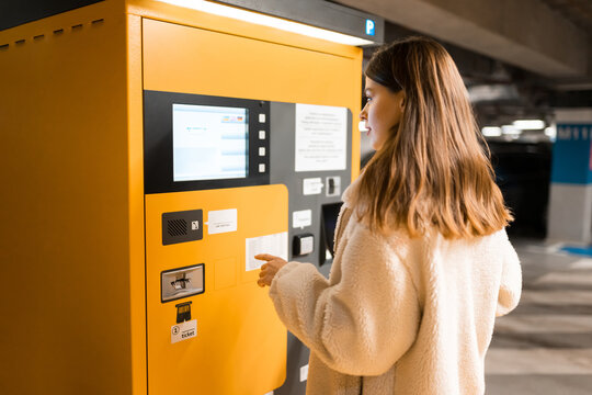 Elegant young girl pays for ticket in parking meter. Woman near terminal in the underground parking