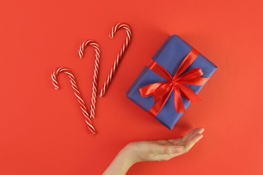 christmas gift on red background with hand. Concept holiday atmosphere, new year, celebration, greeting card. Flatlay, top view