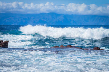 
turquoise ocean breaking waves against black beach and black rocks on a beautiful sunny day