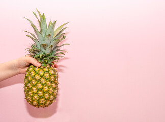 Close-up photo of a young boy holding fresh, ripe pineapple fruit in his hands isolated on a pink wall background in the studio. Appropriate healthy nutrition, vitamin concept. Trial copy space
