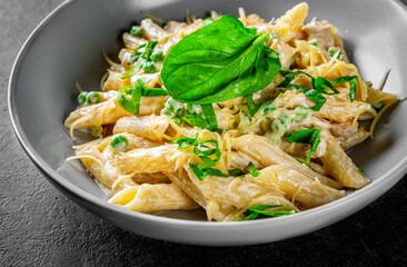 Penne pasta with chicken meat, cream sauce and cheese in a bowl on Dark grey black slate background