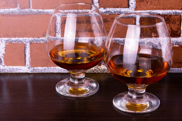 Two glasses with cognac on a brick wall background.