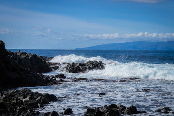 Fototapeta na wymiar turquoise ocean breaking waves against black beach and black rocks on a beautiful sunny day