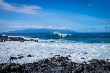 Fototapeta na wymiar turquoise ocean breaking waves against black beach and black rocks on a beautiful sunny day