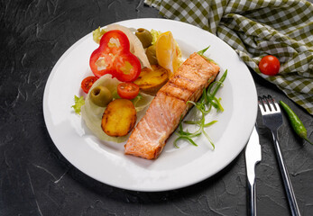 salmon steak with baked and fresh vegetables on a white plate and dark background. Grilled seafood. For the restaurant menu