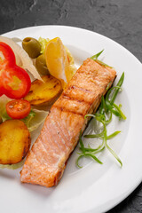salmon steak with baked and fresh vegetables on a white plate and dark background. Grilled seafood. For the restaurant menu