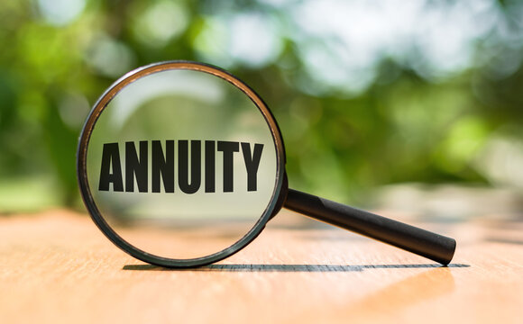 Magnifying glass with text ANNUITY on wooden table and green background.