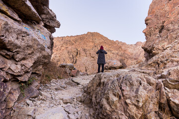 A female tourist standing on the peak of a rocky mountain looking at the ridge in Darband valley in autumn in dawn against colorful sky in the Tochal mountain.