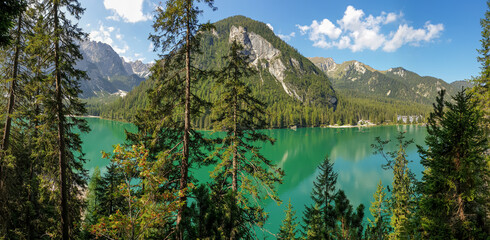 A panoramic view on the Pragser Wildsee, a lake in South Tyrolean Dolomites. High mountain chains around the lake. The sky and mountains are reflecting in the lake. Dense forest at the shore. Serenity