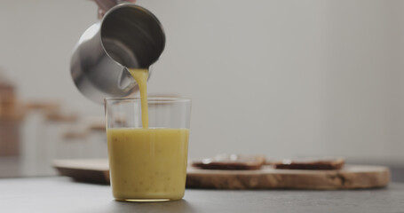 pour mango lulo smoothie into tumbler glass on concrete countertop with copy space