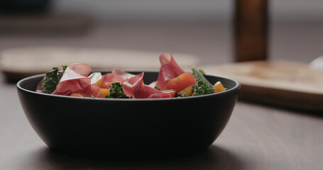salad with kale, coppa and cherry tomatoes from black bowl on concrete countertop