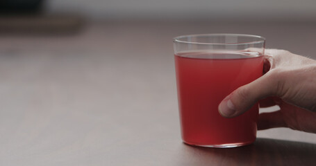 man hand take pink fizzy drink in a tumbler glass from walnut table