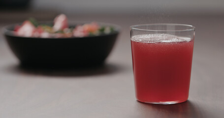 pink fizzy drink in a tumbler glass on walnut table with salad on background
