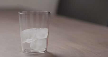 add ice into tumbler glass on walnut table with copy space