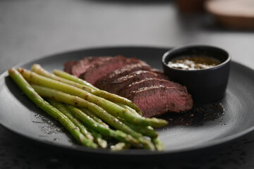 New york steak with asparagus on black plate with pesto sauce