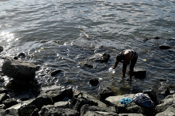 Homeless Mature woman bathing on rocky ocean beach using dipper. silhouettes