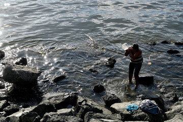 Homeless Mature woman bathing on rocky ocean beach using dipper. silhouettes