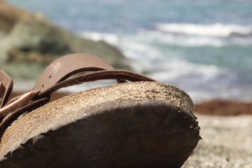 Fototapeta na wymiar Sandal sitting on the sand of a beach close to the waterline and wave
