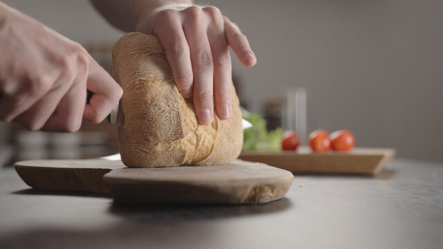 Man slicing small ciabatta bun for sandwich on kitchen countertop
