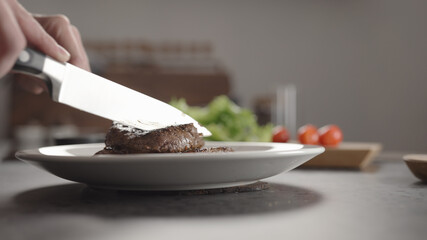 Closeup man slicing steak on white plate on kitchen countertop