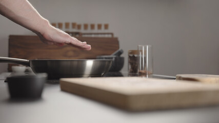 Man checking temp of steel pan on electric hob on kitchen with hand