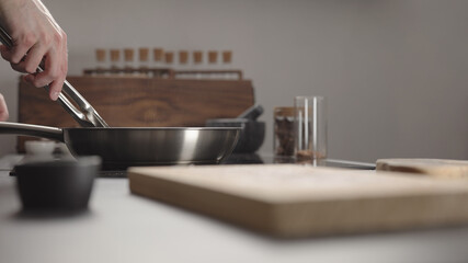 Man flip beef steak with tongs on steel pan on electric hob on kitchen