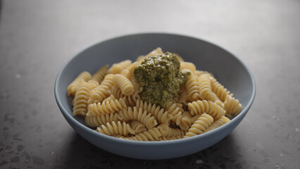pesto to boiled fusilli pasta in blue bowl on concrete background
