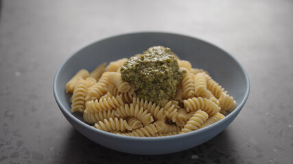 pesto to boiled fusilli pasta in blue bowl on concrete background