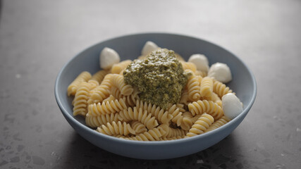 add mozzarella balls to pesto fusilli pasta in blue bowl on concrete background